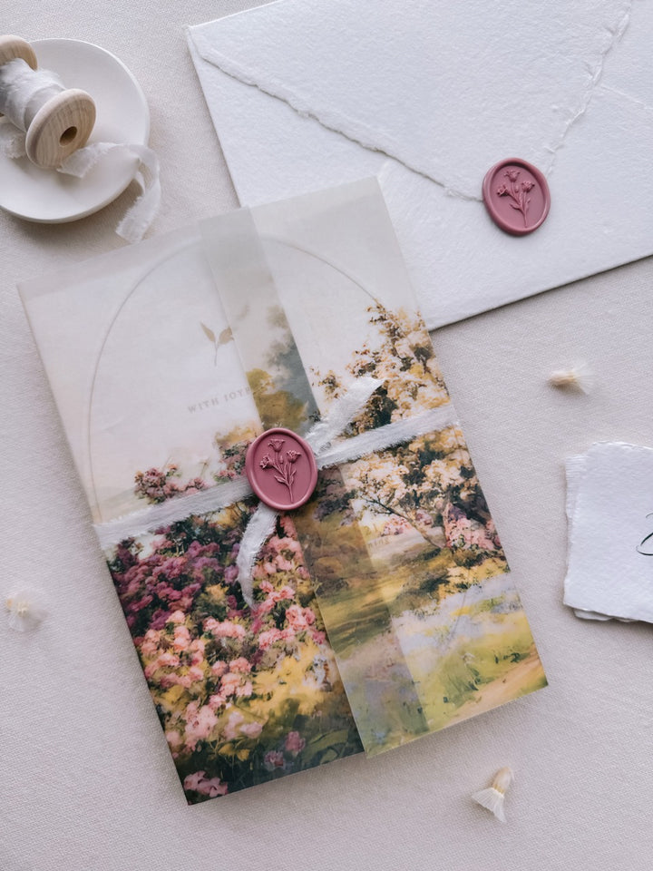 Mauve pink tulip oval wax seal on a watercolor garden-themed vellum wrap tied with white silk ribbon, set against a wedding invitation suite.