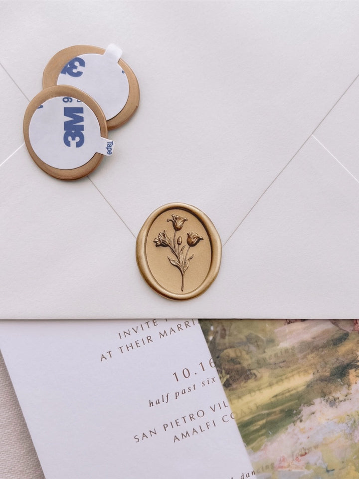 Gold pre-made tulip oval wax seal stickers with self-adhesive backings on a beige envelope, set against a white wedding invitation card and watercolor vellum jacket.