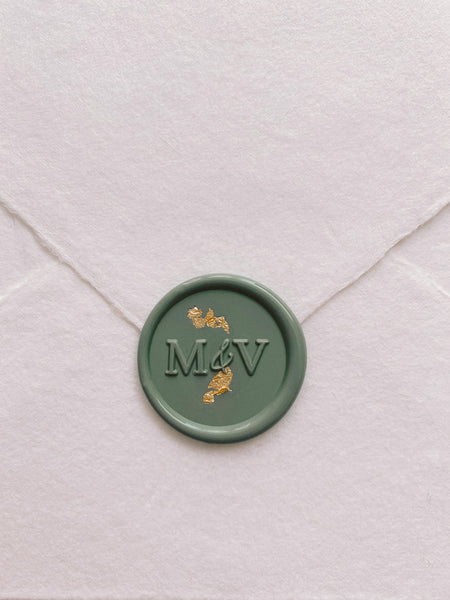 Typeface monogram round wax seal in dark sage green embellished with gold flakes on handmade paper envelope_front angle