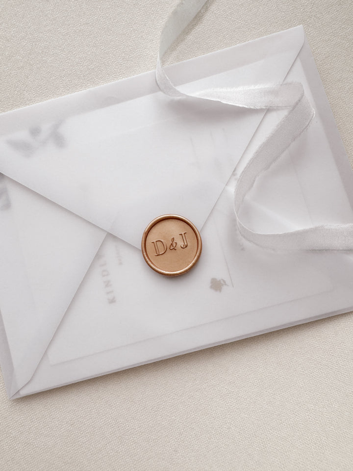Modern typeface monogram wax seal in color peachy gold on a vellum envelope