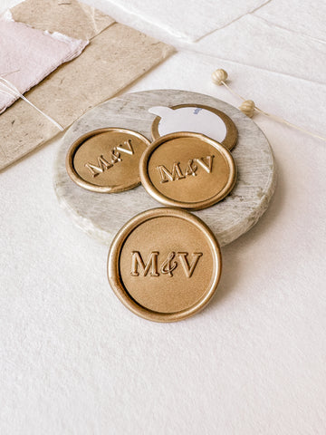 Typeface monogram custom wax seals in gold styled with a small gray stone dish, handmade paper and a dried floral branch