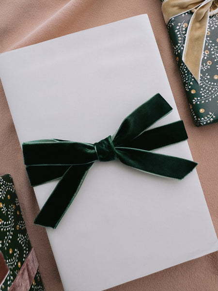 beige gift wrap tied with a dark green velvet ribbon bow