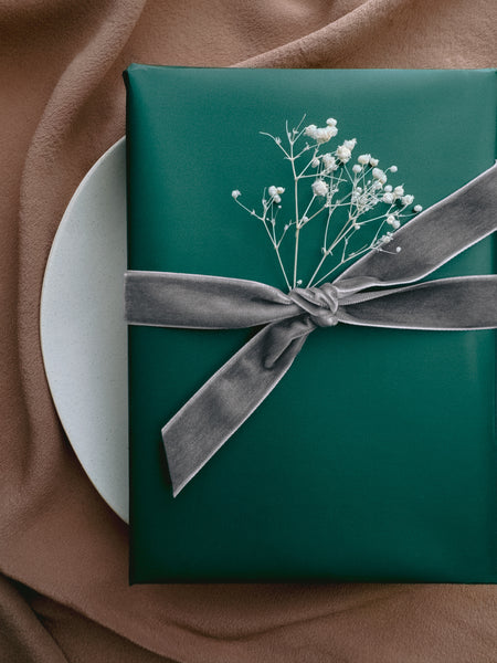 green Christmas gift wrap decorated with silver velvet ribbon bow and a dried floral branch