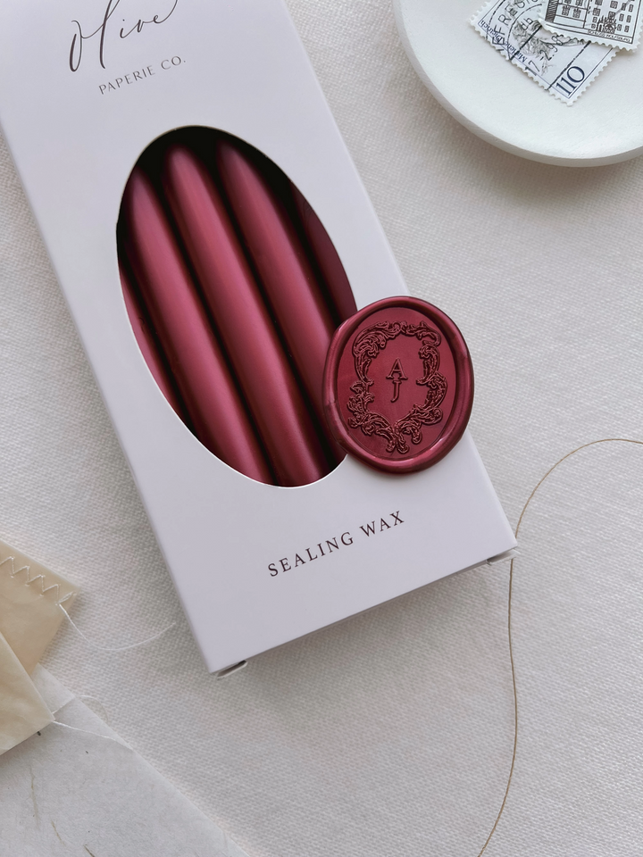 Dark metallic red vintage Baroque crest monogram oval wax seal on a box of metallic red sealing wax sticks