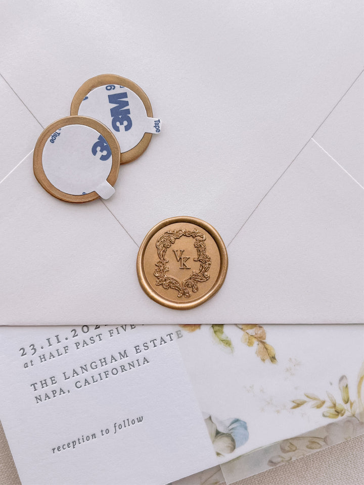 vintage crest monogram gold wax seal stickers with self-adhesive backings on a wedding invitation, beige envelope, and floral vellum jacket