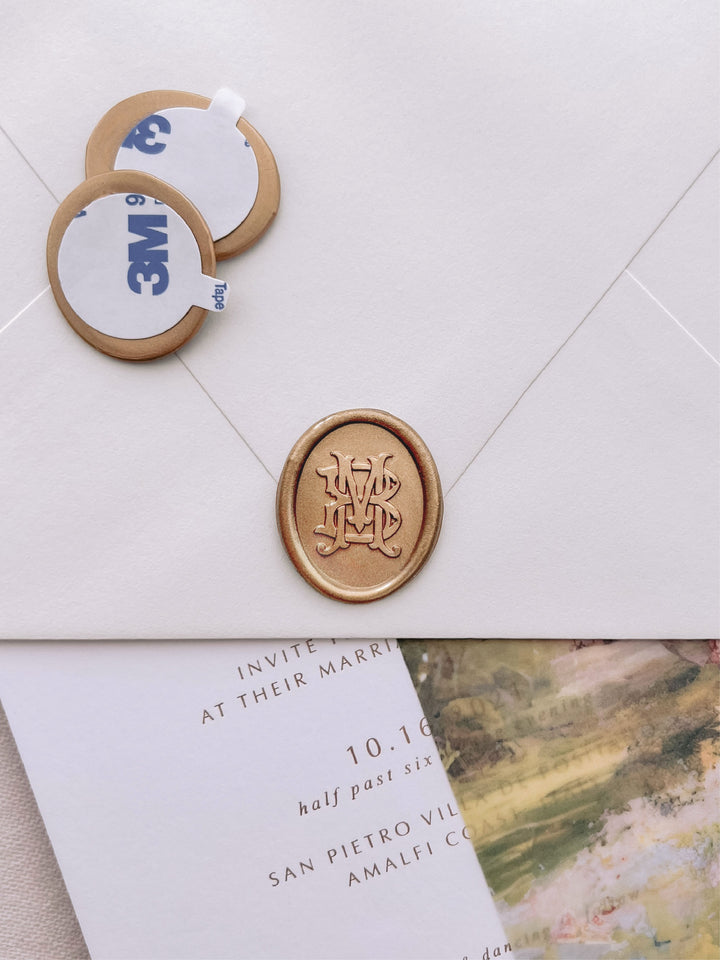vintage interlocked monogram oval gold wax seal stickers with self-adhesive backings on a wedding invitation, beige envelope, and floral vellum jacket