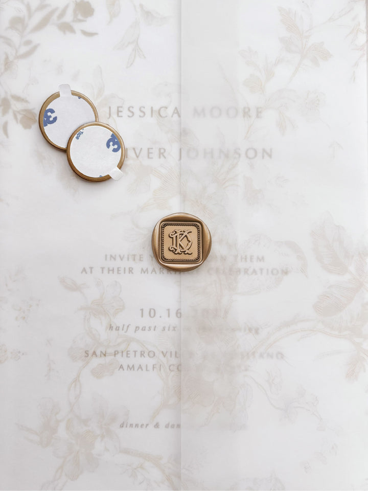 Gold vintage interlocked monogram border design square wax seals with adhesive backings on a beige floral print wedding invitation vellum jacket 