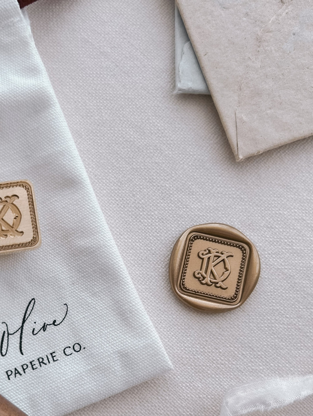 Personalized initials gold vintage square border wax seal featuring a custom monogram on a light beige background with a wax stamp head on a white pouch.