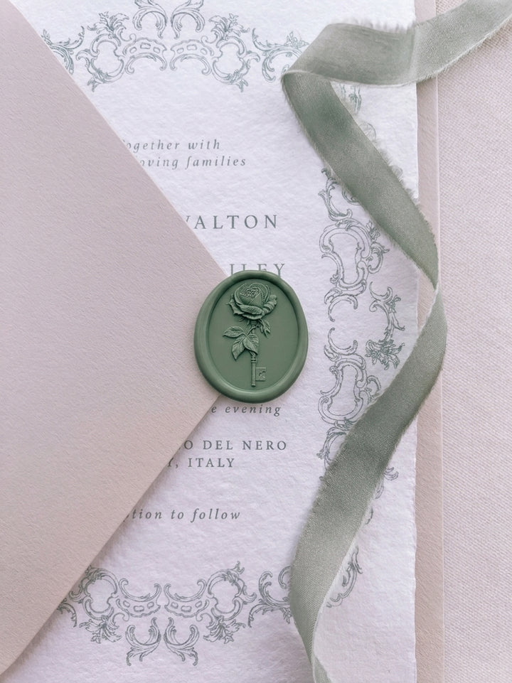 Sage green rose and key wax seal securing a blush beige wedding envelope, layered over an ornate baroque wedding invitation card with sage green silk ribbon detail.
