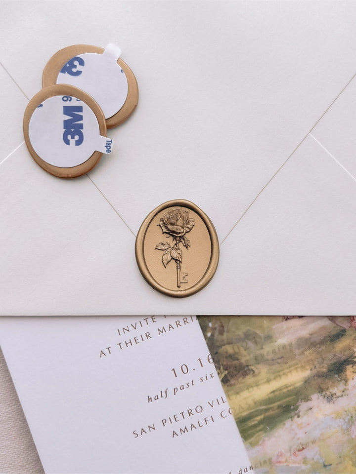 Gold rose and key wax seal stickers with 3M adhesive backing displayed beside a sealed ivory wedding envelope over a watercolor vellum jacket and wedding invitation card