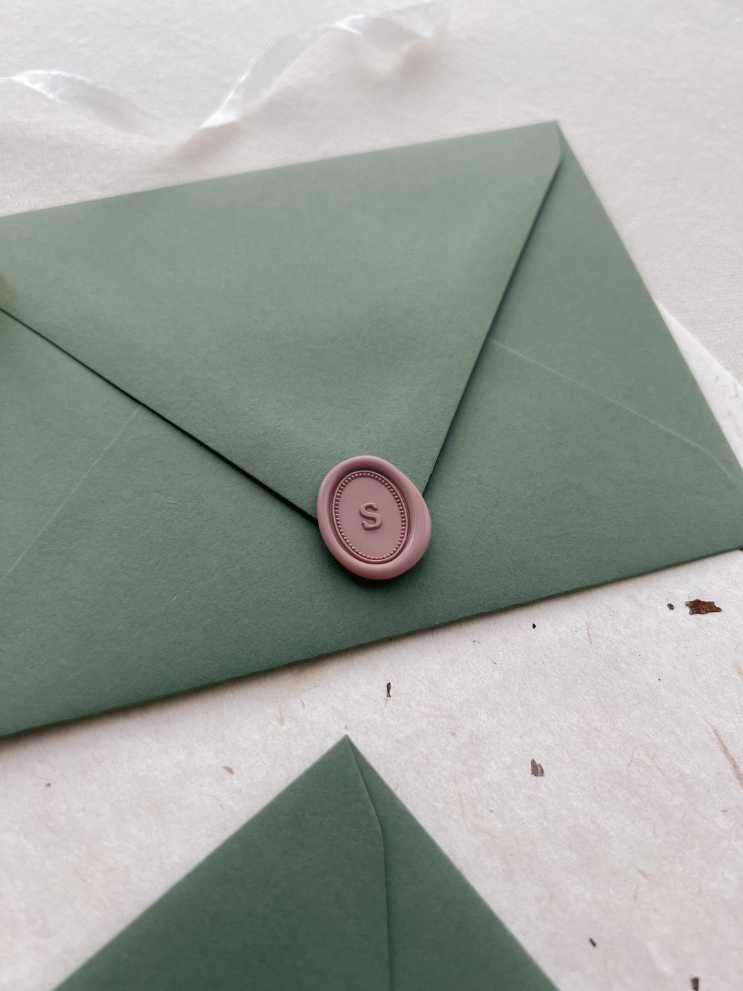 soft rose colored custom initial mini oval wax seal on an olive green envelope