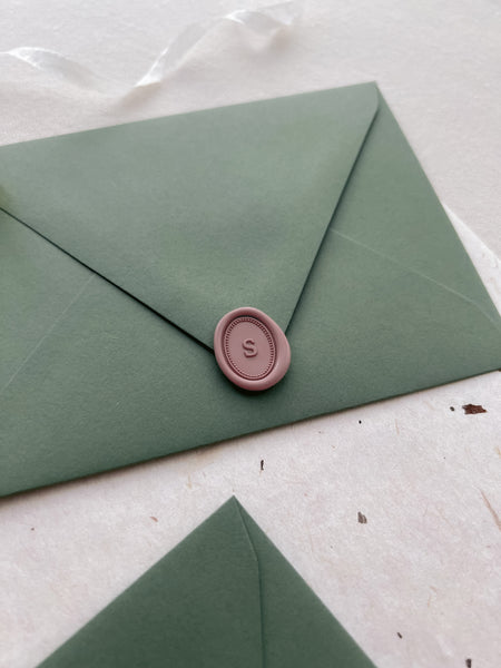 soft rose colored custom initial mini oval wax seal on an olive green envelope