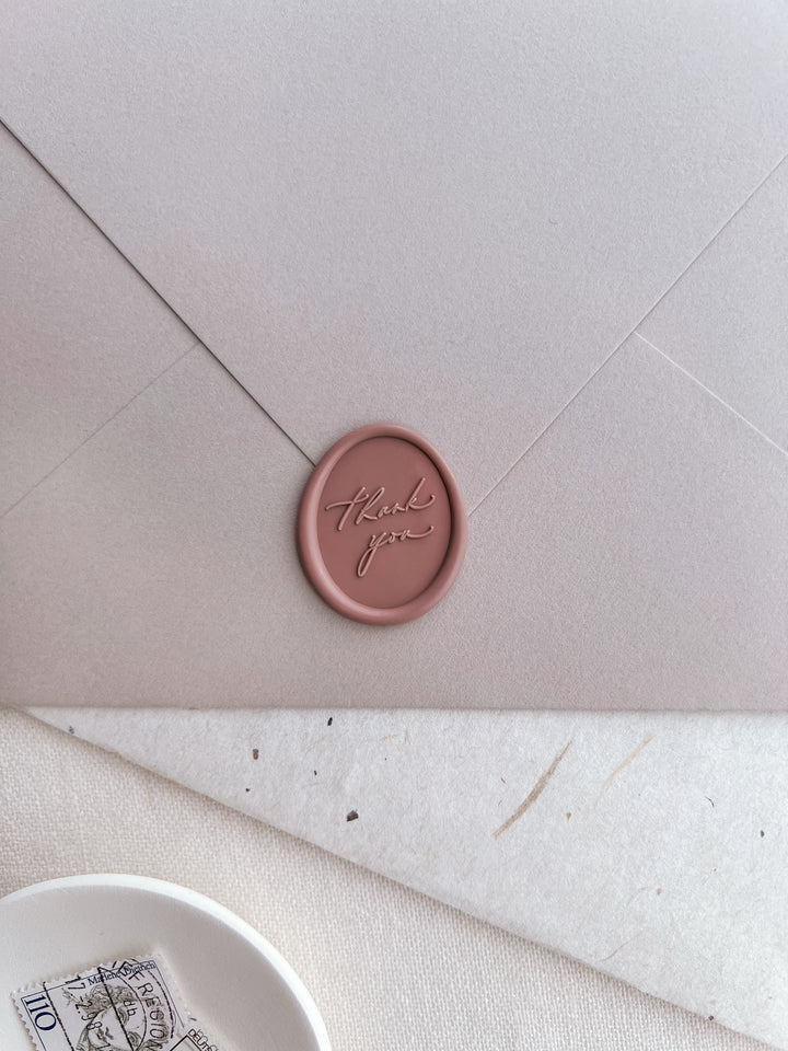 soft rose colored oval thank you wax seal on a pinkish beige envelope