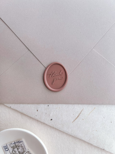 soft rose colored oval thank you wax seal on a pinkish beige envelope