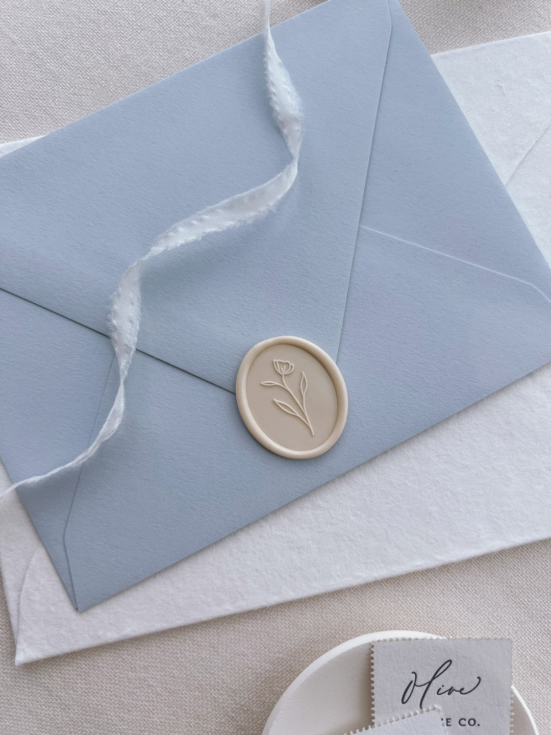 Light beige simple flower design oval wax seal on a light blue envelope