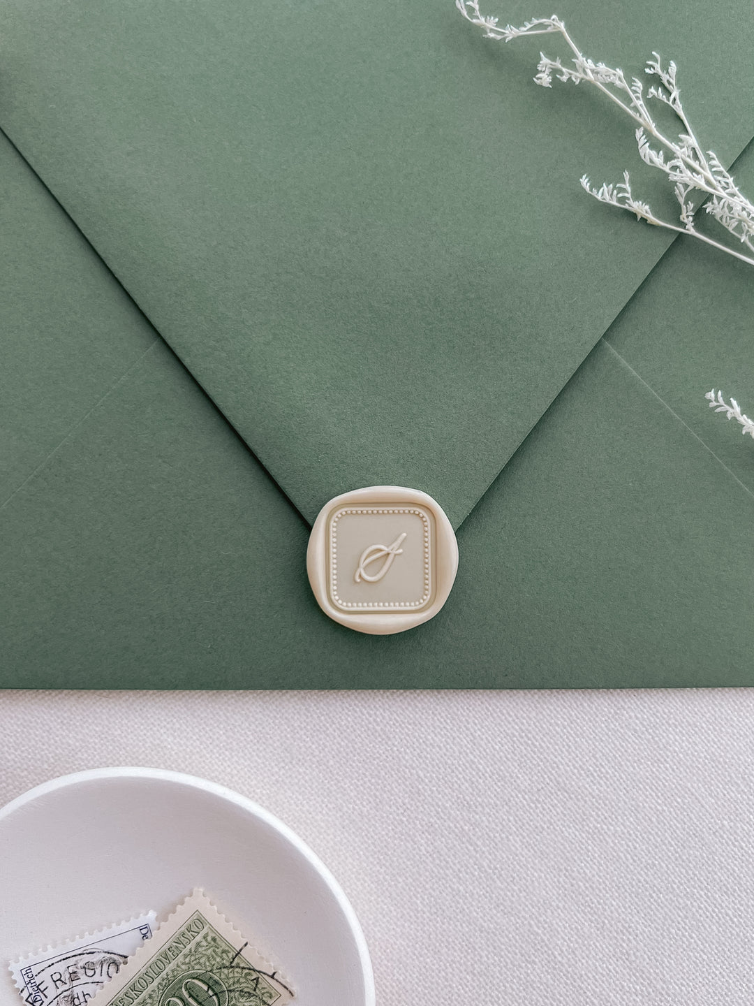 Light beige square shaped custom  initial wax seal on an olive green envelope