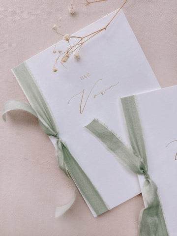 A set of two His and Her gold foil white vow books in calligraphy script with sage colored silk ribbon