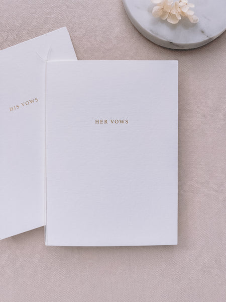 A set of two His and Her gold foil white card stock vow books in typeface font with fine white twine