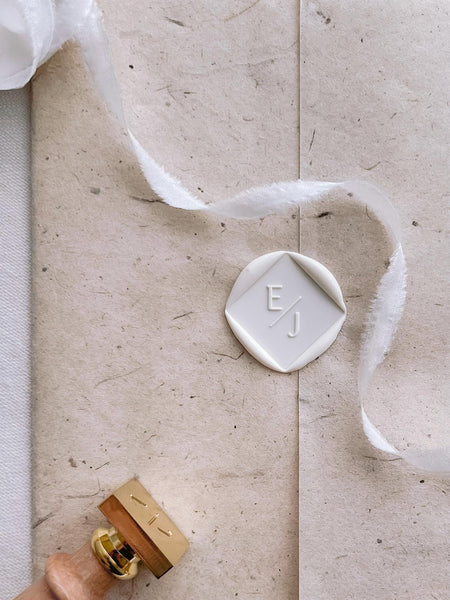 Soft white square shaped custom monogram wax seal on a brown texture wedding invitation wrap 