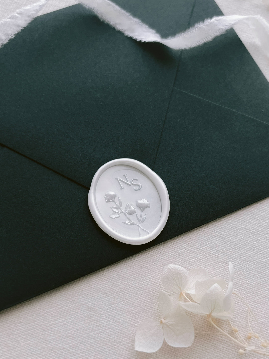 Pearl white custom monogram floral design oval wax seal on a dark green envelope