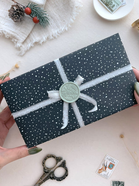 Light sage green festive wax seal featuring a wintery botanical design, decorated on a wrapper Christmas gift